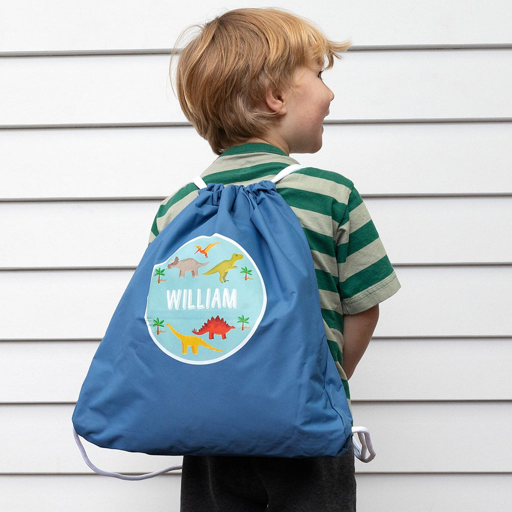 Child wearing personalised drawstring swim bag featuring dinosaur design and their name.