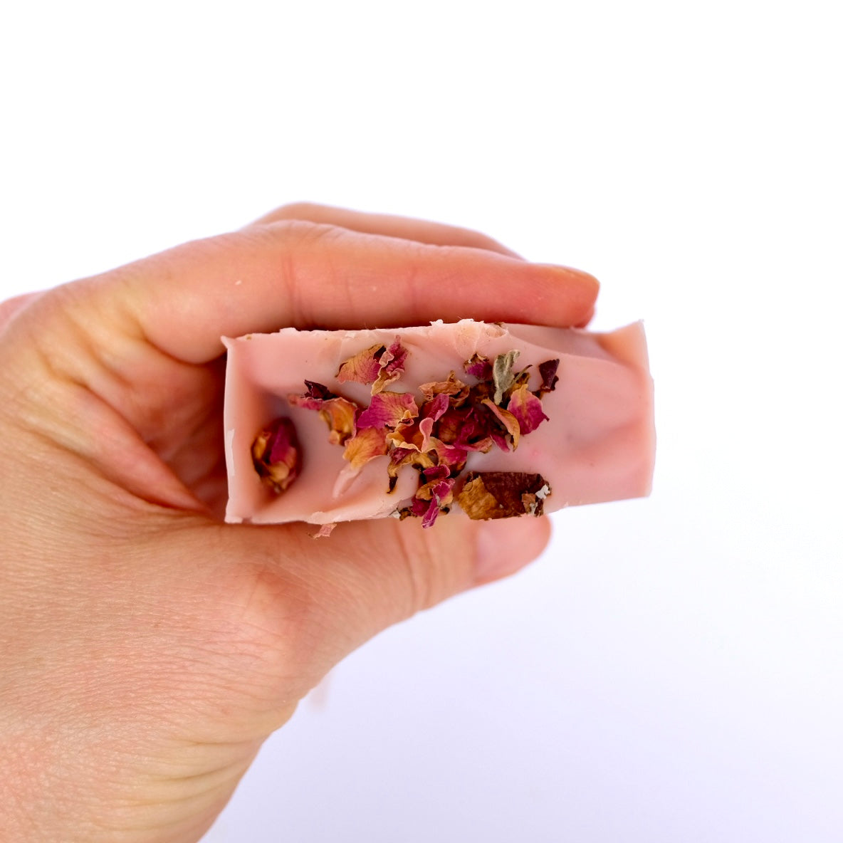 Hand holding a bar of tallow soap with dried flowers on a white background