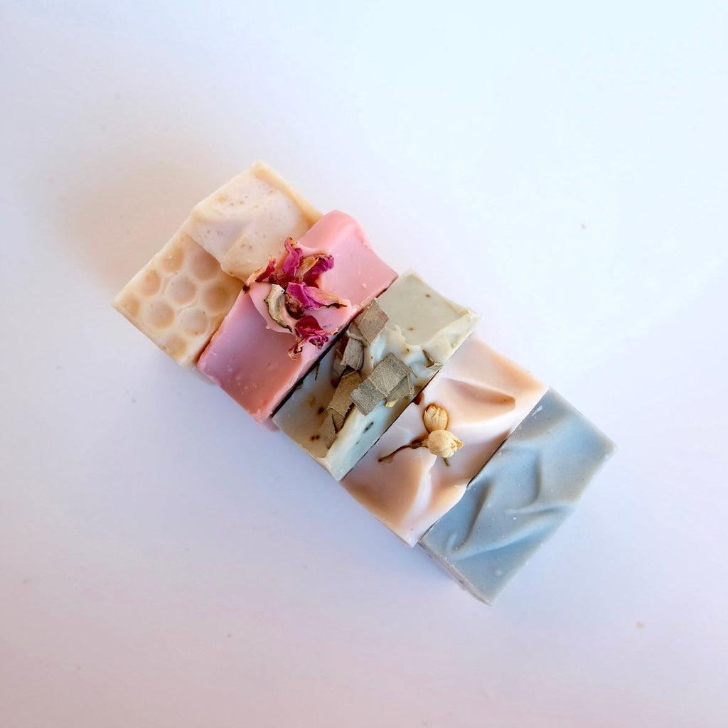 five rectangular tallow soap bars with different textures and colours on a white background