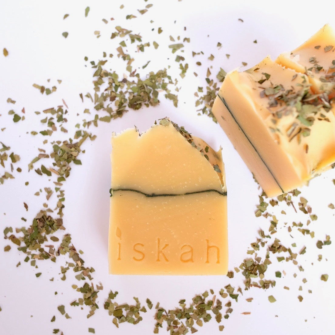 bars of lemon myrtle tallow soap sitting on a white background surrounded by lemon myrtle leaves crushed