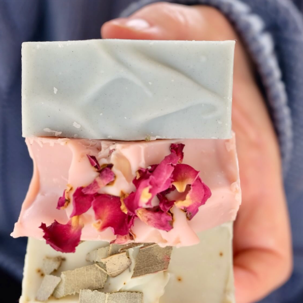 hand holding three tallow soaps one blue, pink and green